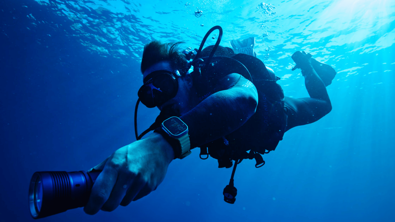 Scuba diver underwater wearing Apple watch ultra 2 on wrist while holding a flashlight camera
