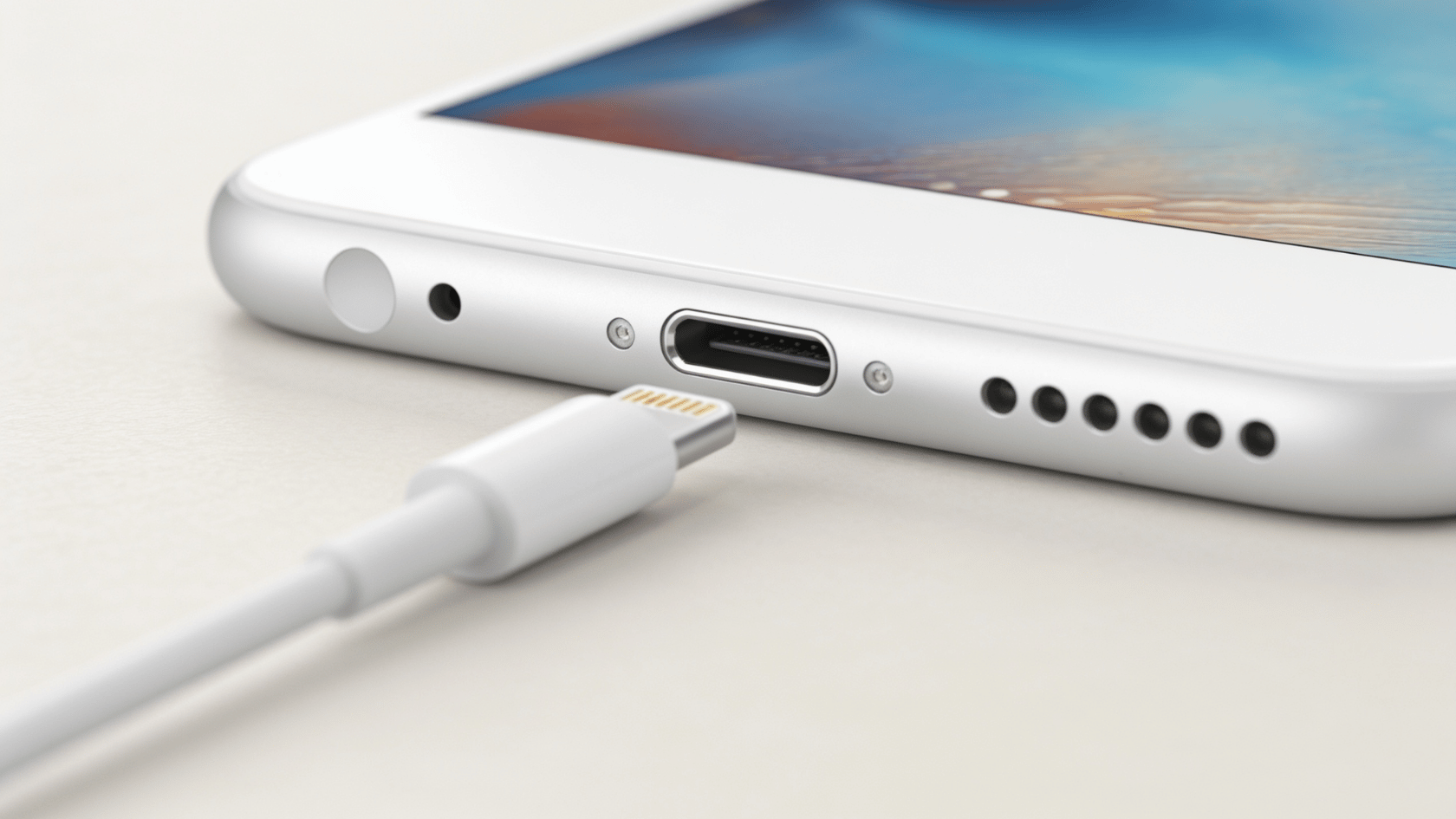 Lightning cable connector plugged into the charging port of a iPhone shown in close-up on a light surface.